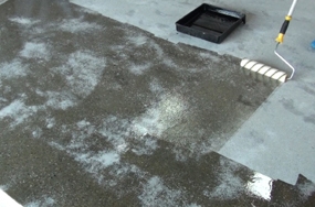 A contractor applying a clear sealer onto a porous concrete slab.