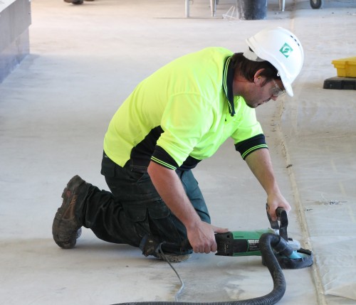 A resin flooring contractor using a grinder on a concrete floor.